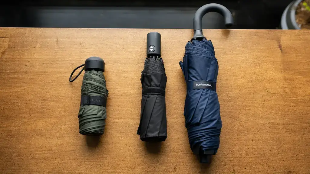 Travel umbrella collapsed and clipped to the outside pocket of a carry-on suitcase near an airport gate